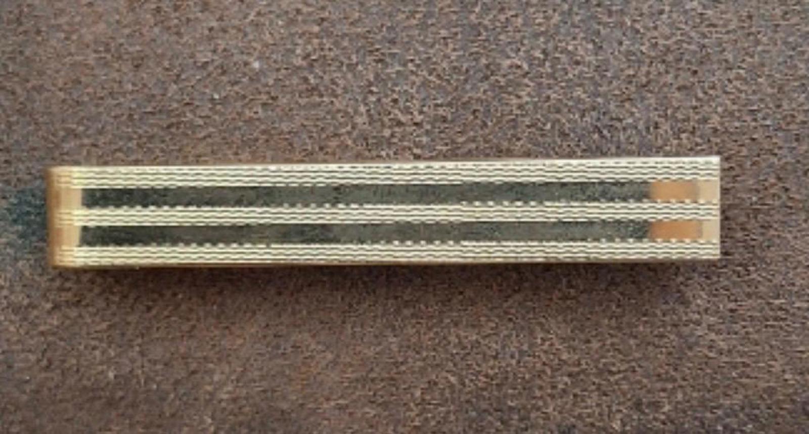 Gold tone striped tie bar clip lying flat on dark fabric