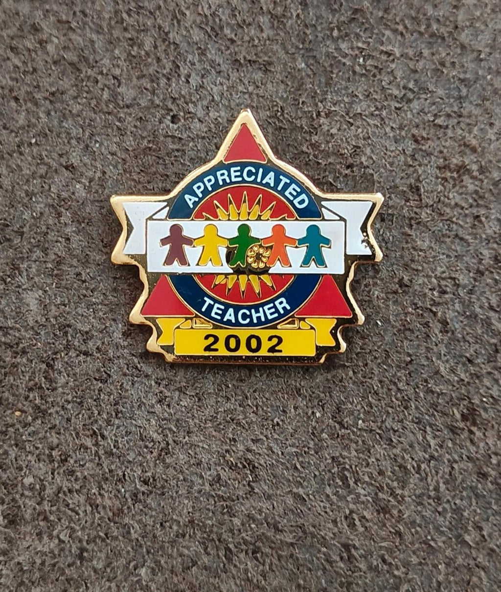Teacher enamel pin with “Appreciated Teacher” and “2002”, red ribbon and blue center