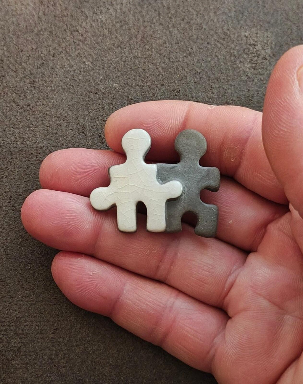 Puzzle buddy brooch set held in hand: white and gray joined figure pieces