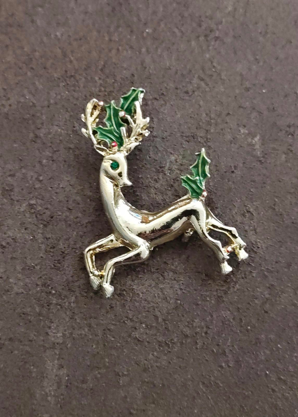 Gold-tone reindeer brooch with green enamel holly, angled view