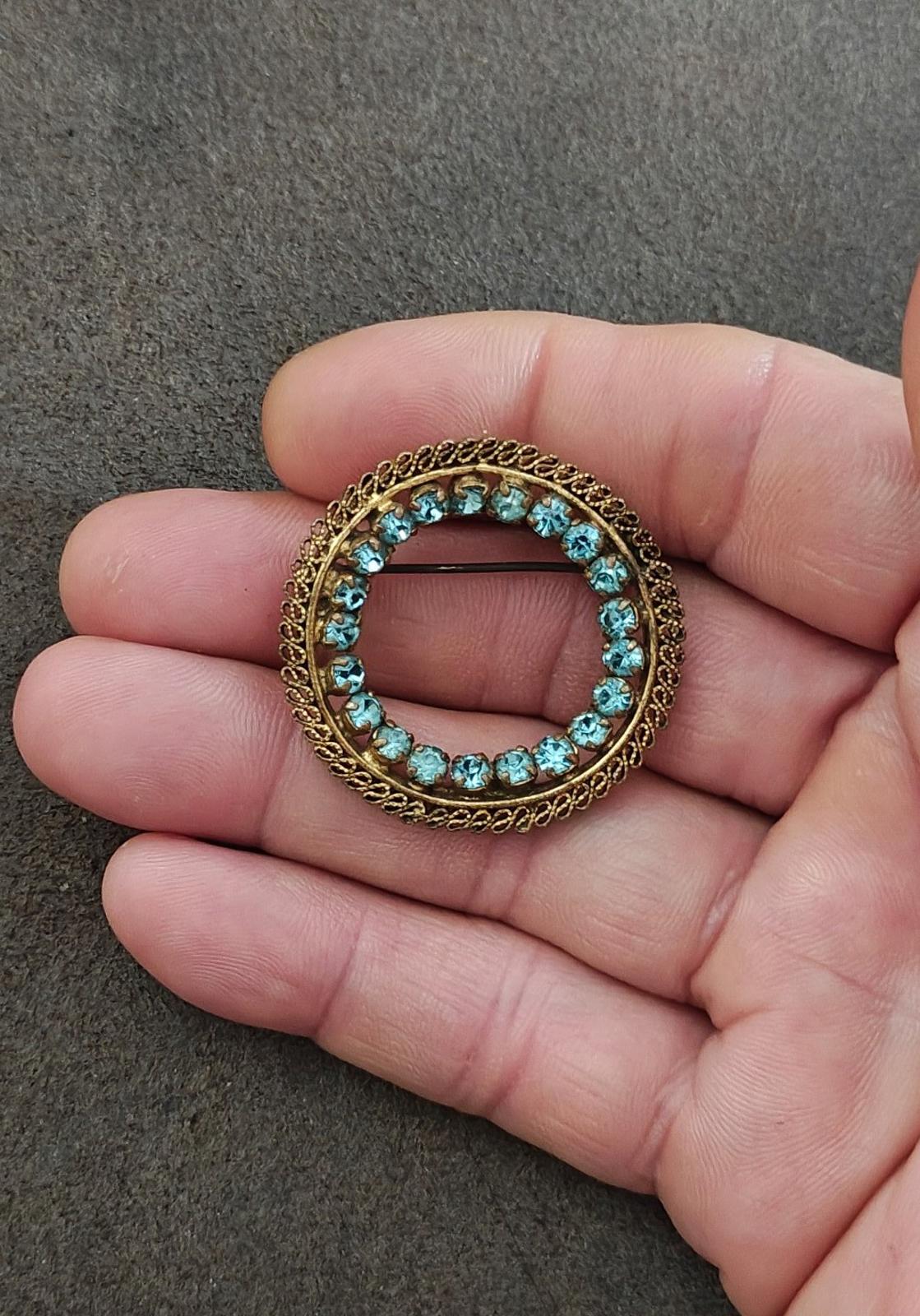 Gold-tone round brooch with blue stones encircling an empty center, handheld