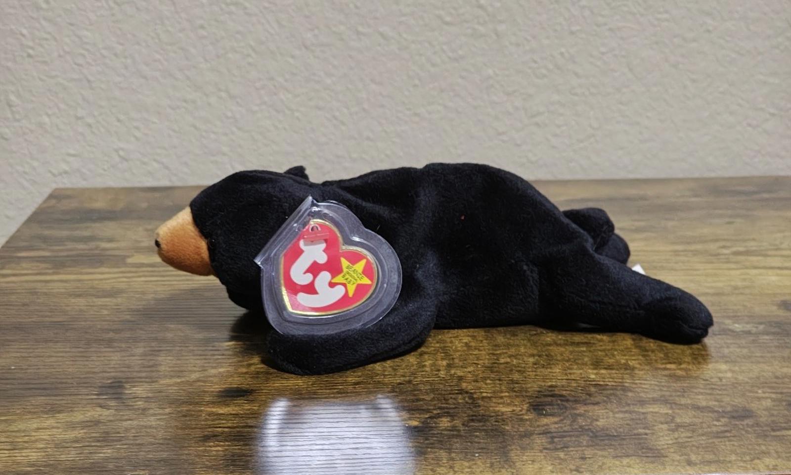 Black plush bear beanbag lying down with round red logo tag on the side
