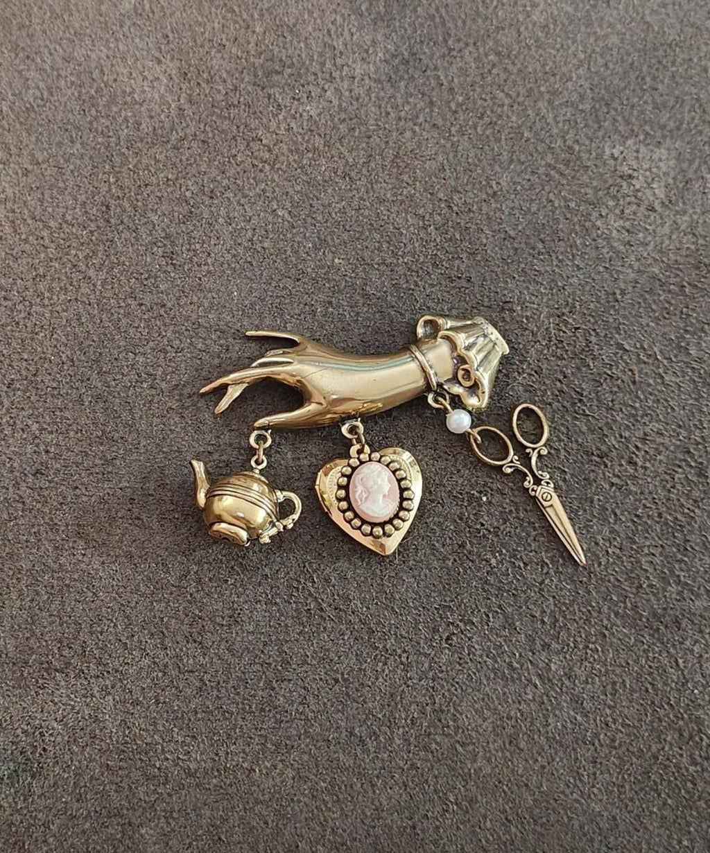 Gold-tone charm dangle brooch laid flat with bird head, teapot charm, heart pendant, and key charm