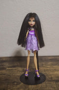 Purple Monster High-style doll in a sleeveless dress with matching purple heels.