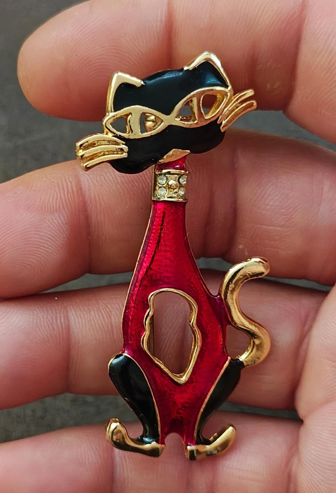 Red and black enamel cat mask brooch with gold-tone whiskers, close-up in hand.