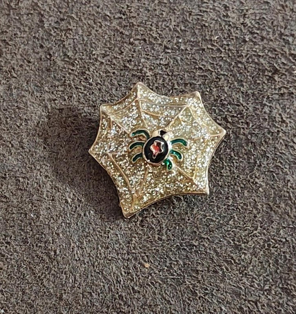 Gold spider web enamel pin with glitter finish, black spider with red oval center and green legs