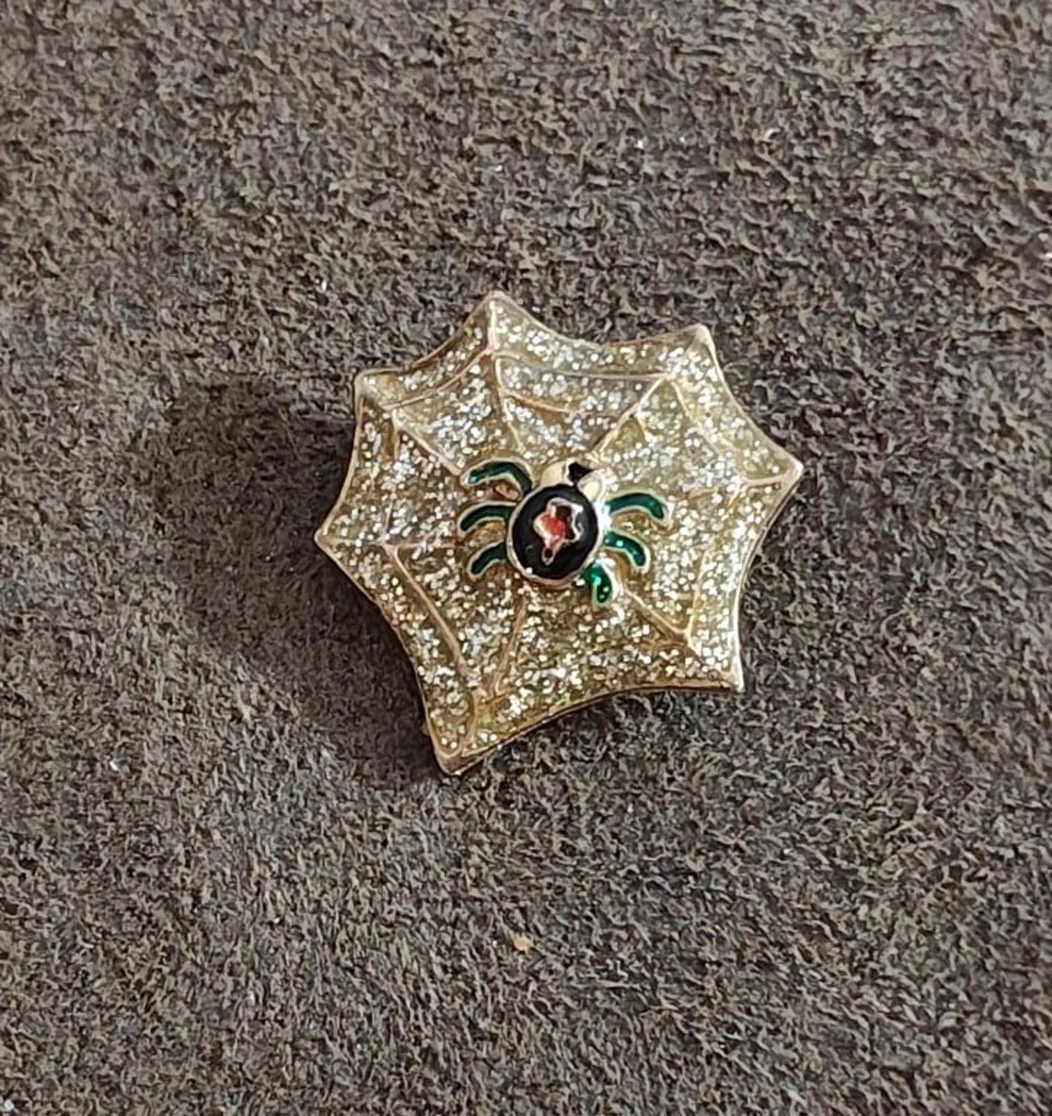 Gold spider web enamel pin with glitter finish, black spider with red oval center and green legs