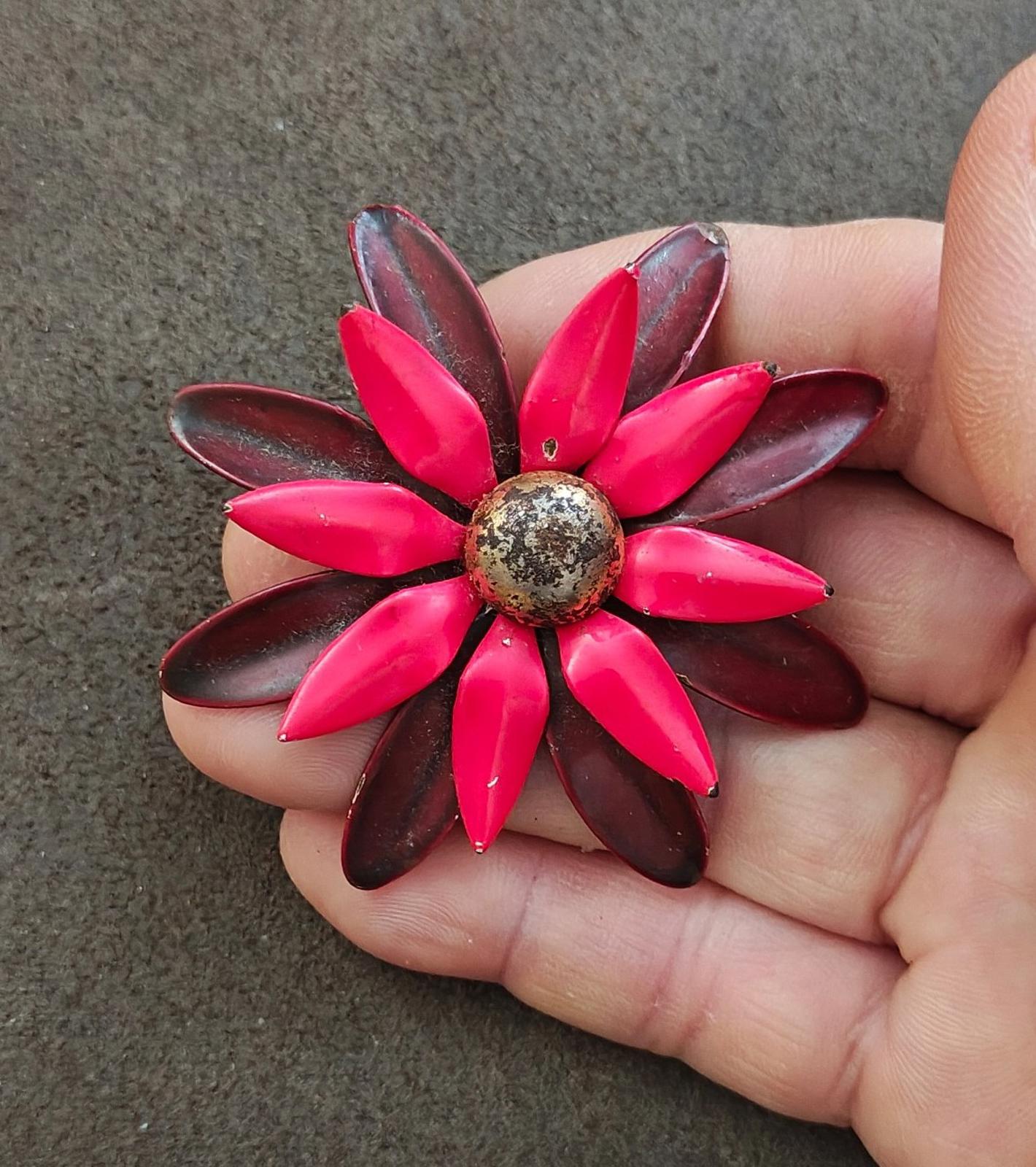 Red and burgundy daisy enamel metal pin with round textured center on hand