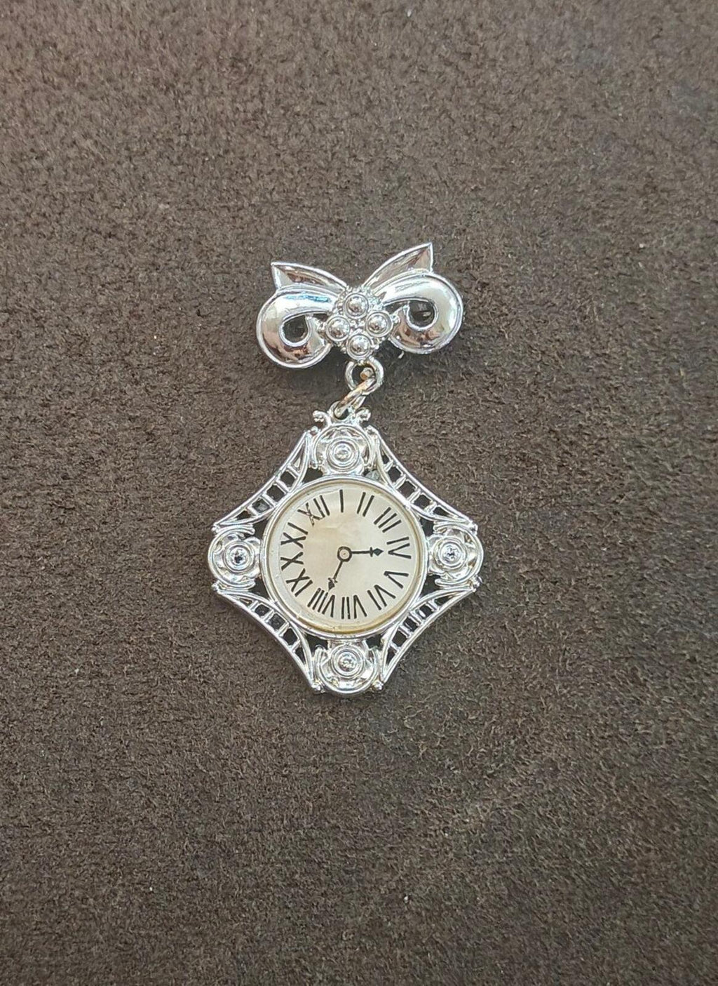 Silver-tone bow clock brooch, standalone view; filigree square pendant with roman numerals.