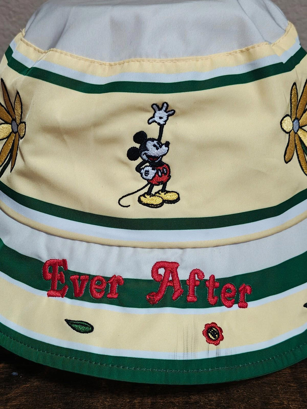 Close-up cream bucket hat with green stripes, Mickey Mouse character and “Ever After” embroidery