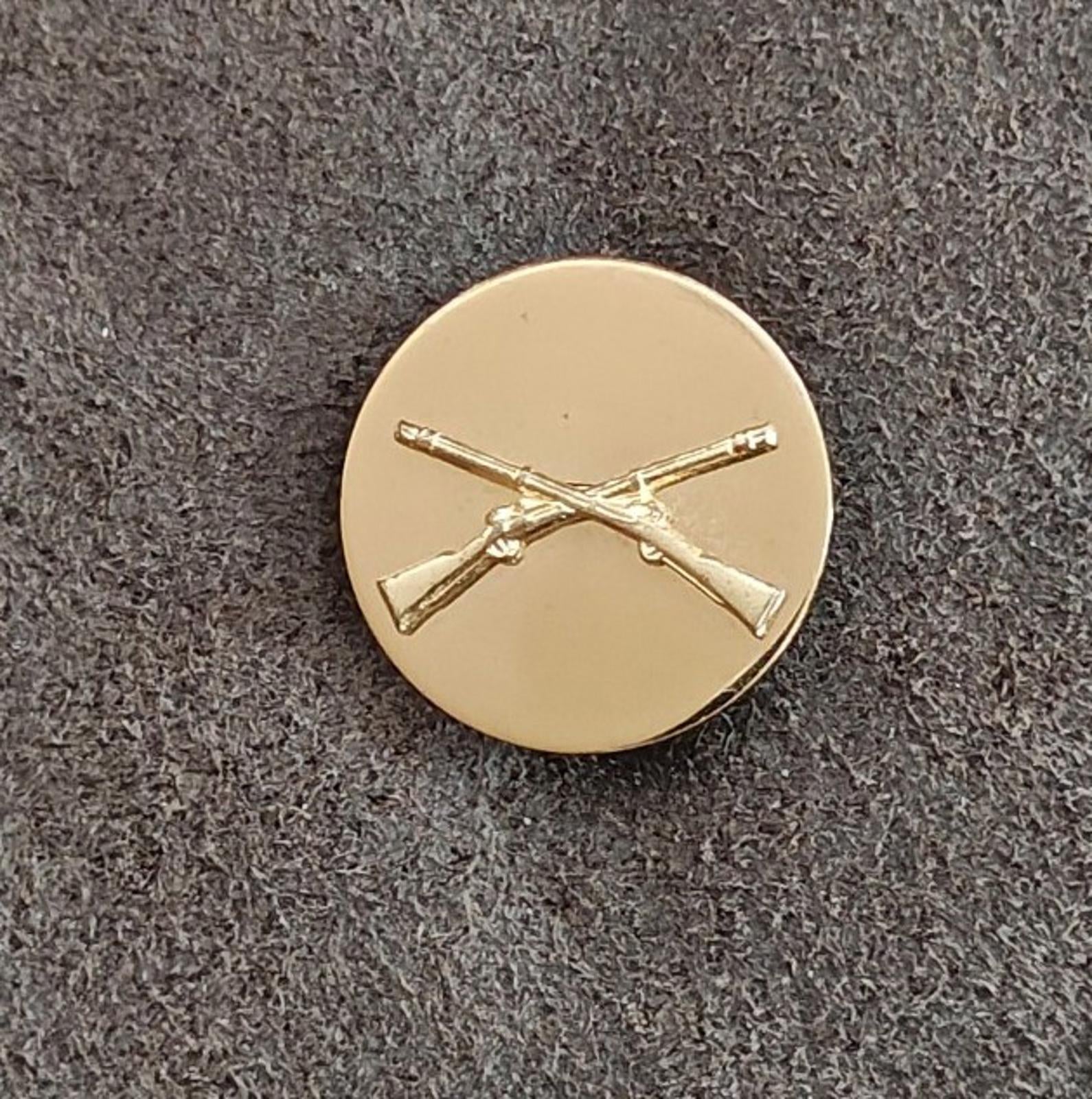 Gold circular brass pin with crossed rifles emblem, front