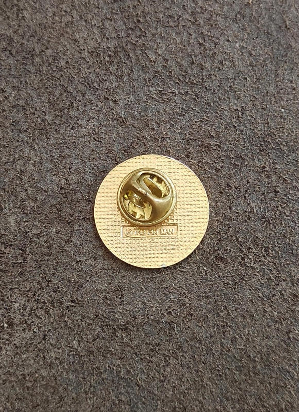 Back of round gold-tone teacher pin with raised clasp and small stamped markings.