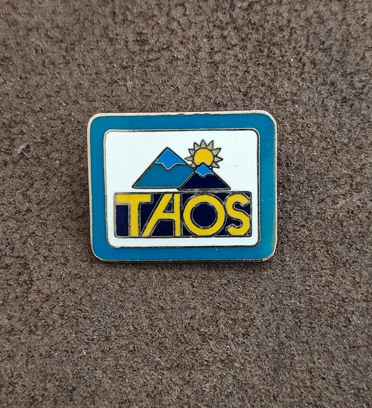 Taos ski valley blue enamel lapel pin with sunburst and mountains; “TAOS” lettering.