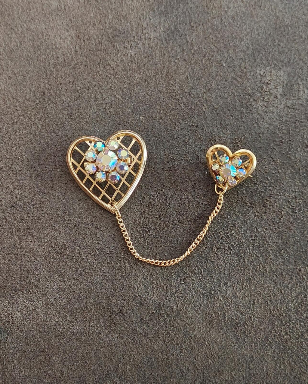 Gold-tone double heart brooch with blue iridescent stones, chain linking the hearts