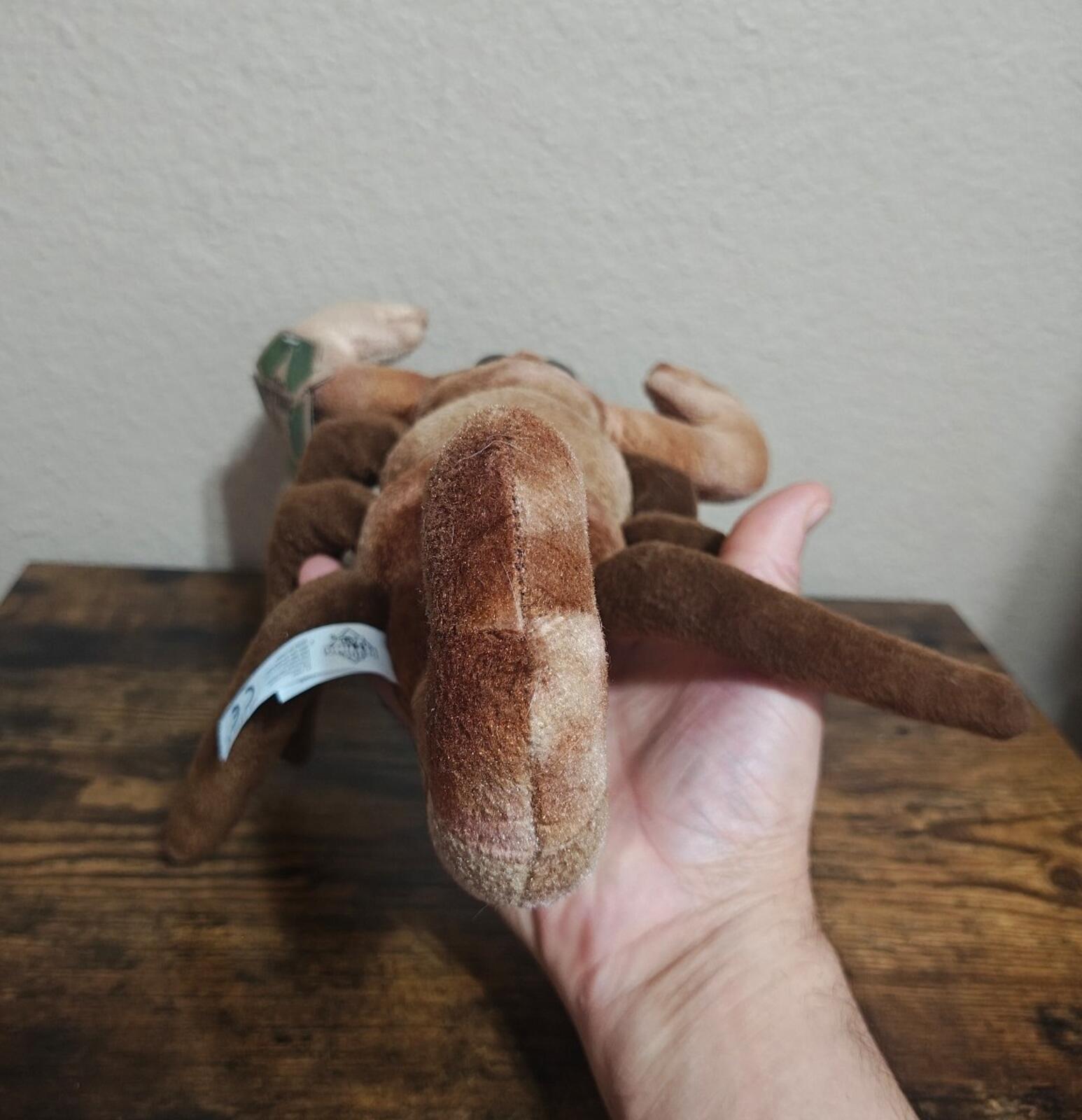 Brown plush scorpion back view in hand, with recycling swing tag near the legs