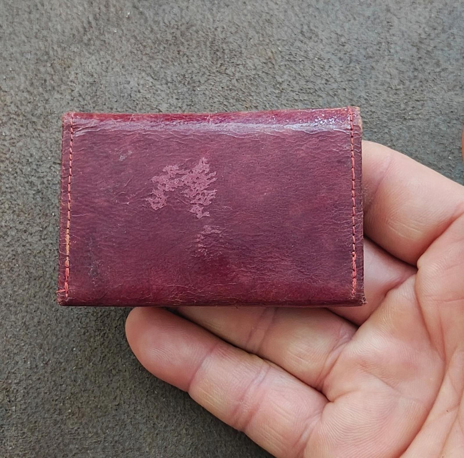 Rectangular burgundy leather coin purse wallet with worn finish and small scuff mark.