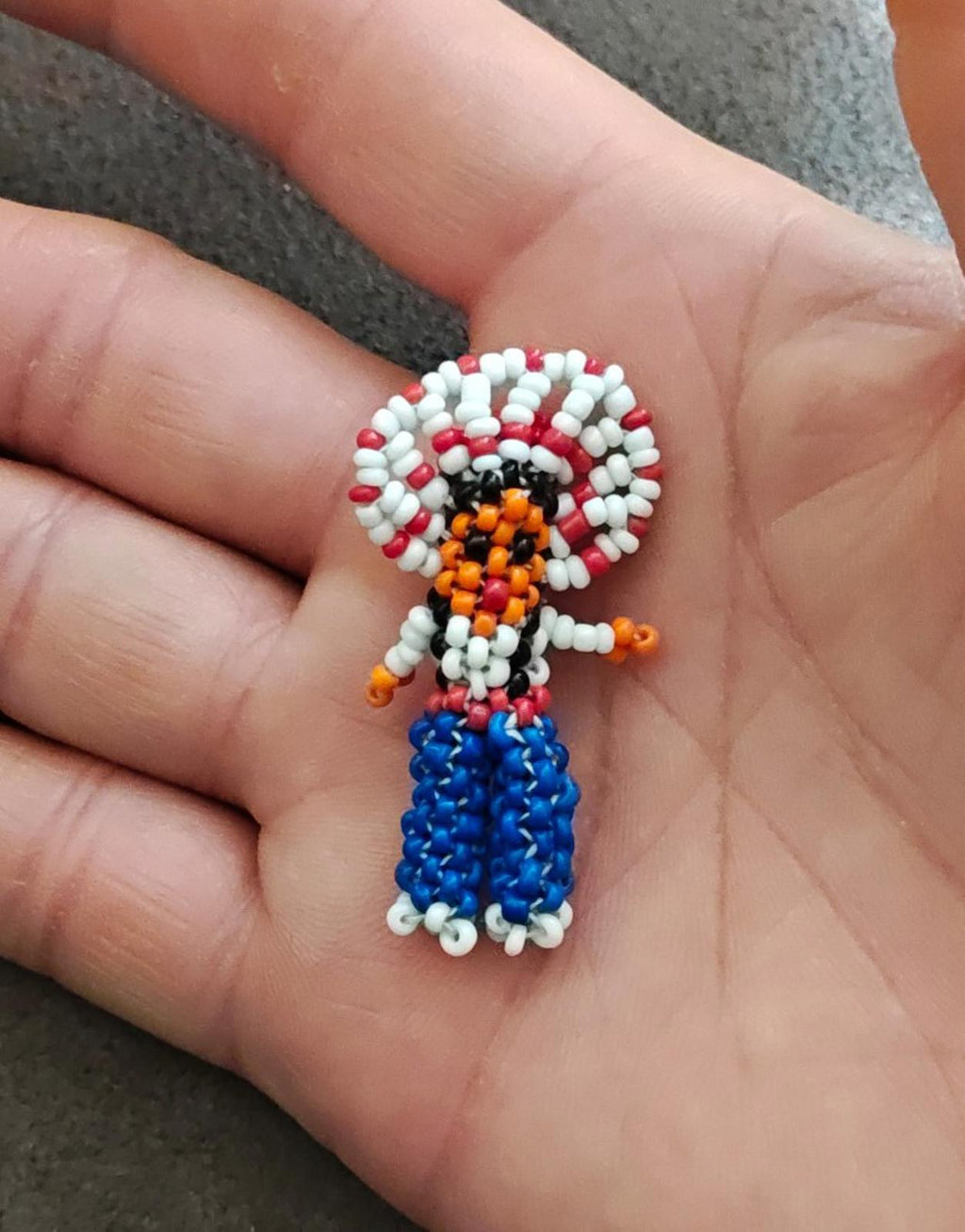 Seed bead figure brooch with red-and-white hair, orange face, and blue beaded dress