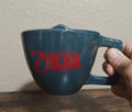 Blue Zelda-themed mug with red 'Legend of Zelda' logo on the cup front.