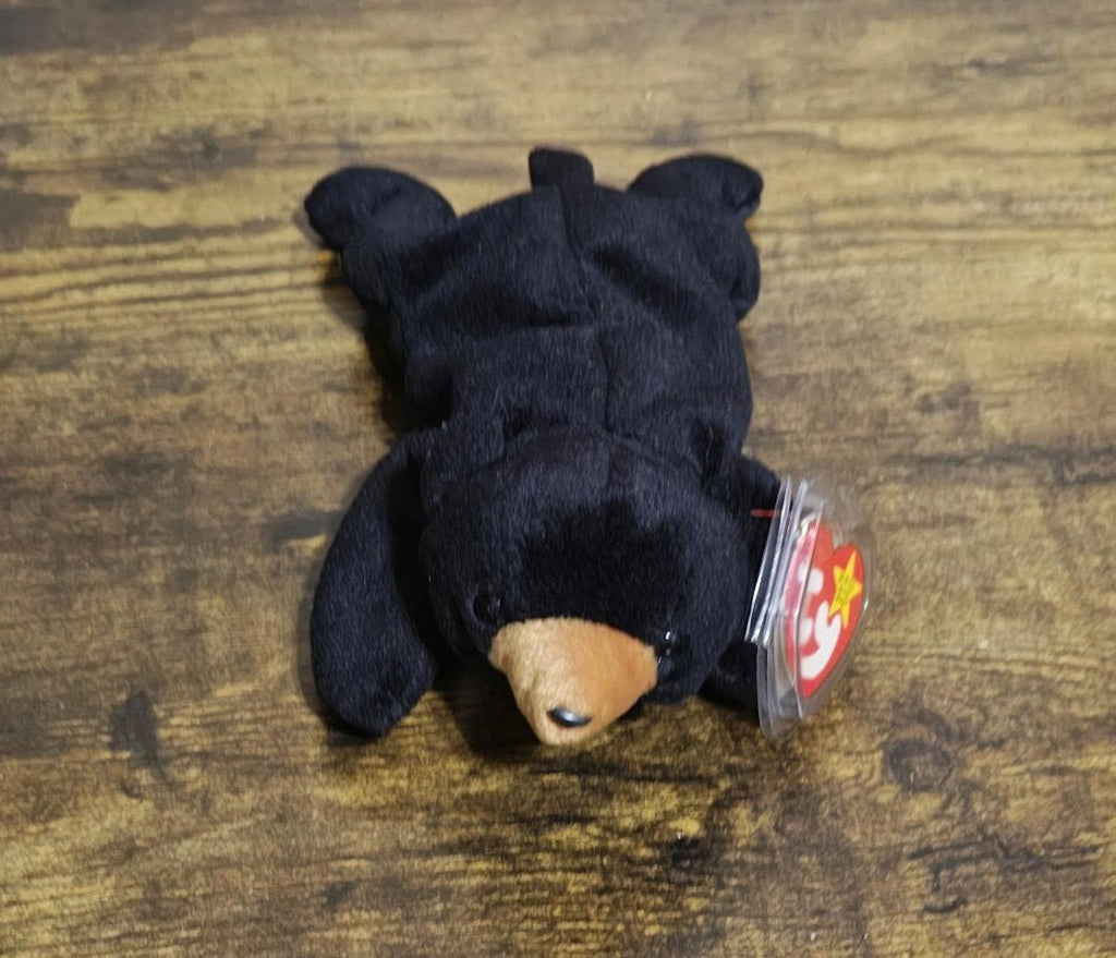 Black plush bear beanbag lying down with red shield logo tag attached