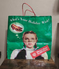 Green paper shopping bag with red handles, “What’s Your Holiday Wish!” and Dorothy