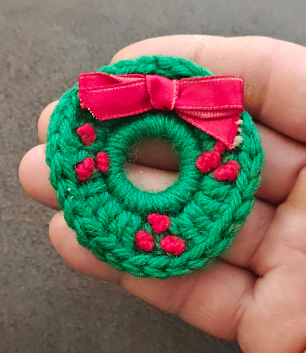 Green knitted wreath brooch with pink bow, red berry accents, round ring front