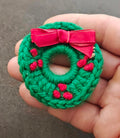 Green knitted wreath brooch with pink bow, red berry accents, round ring front