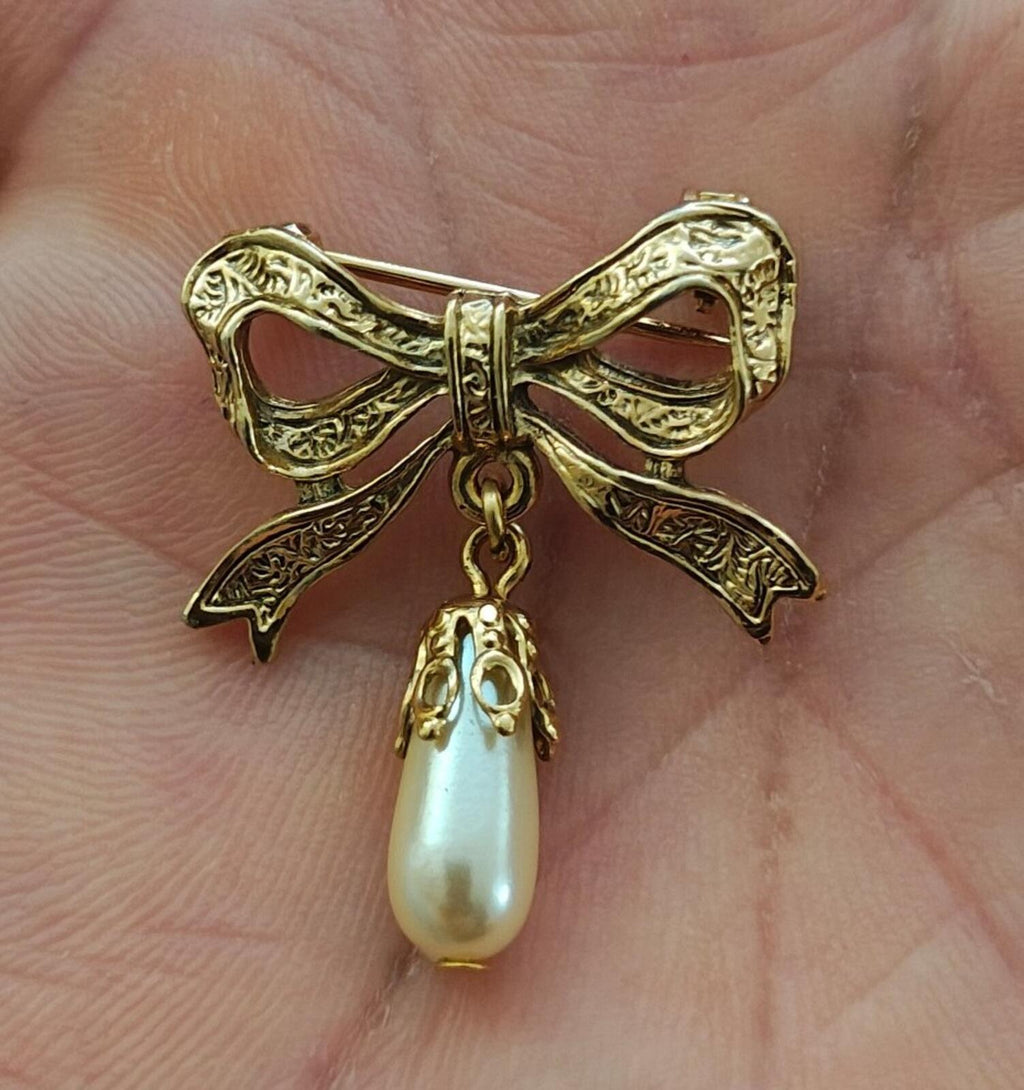 Gold bow brooch with dangling faux teardrop pearl on ornate embossed ribbon frame