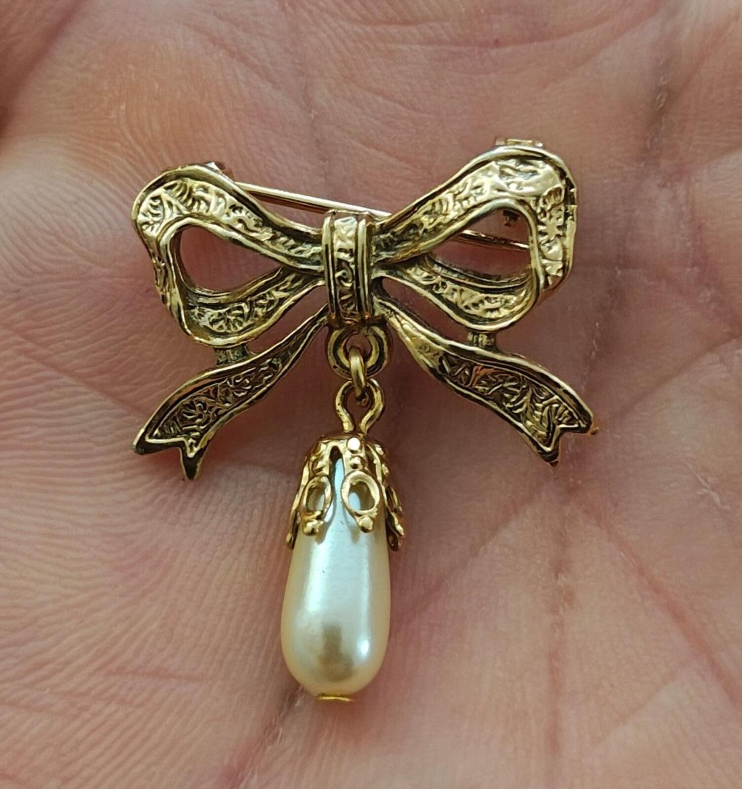 Gold bow brooch with dangling faux teardrop pearl on ornate embossed ribbon frame