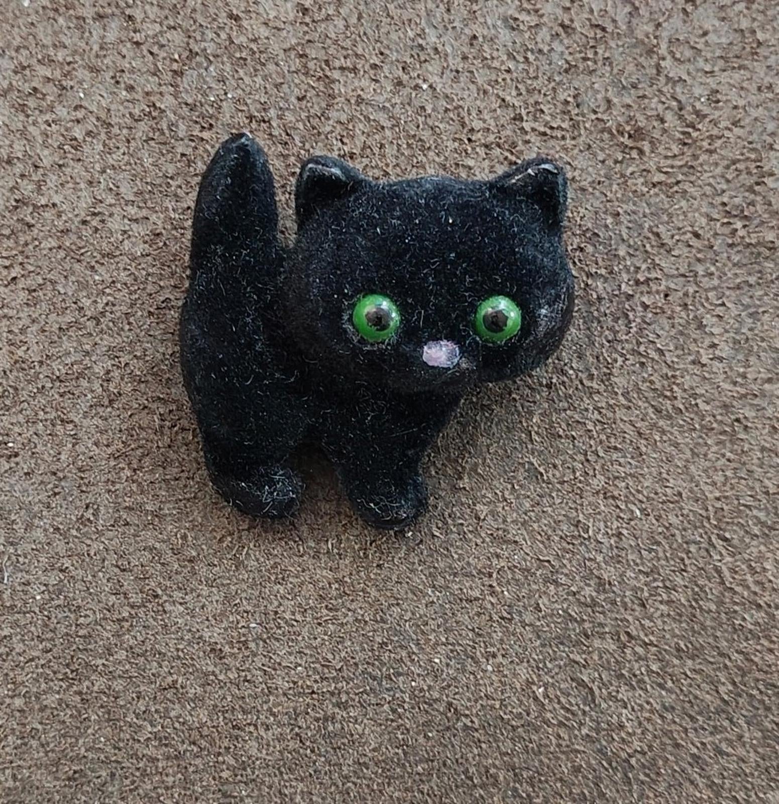 Black fuzzy cat brooch with green eyes, angled view