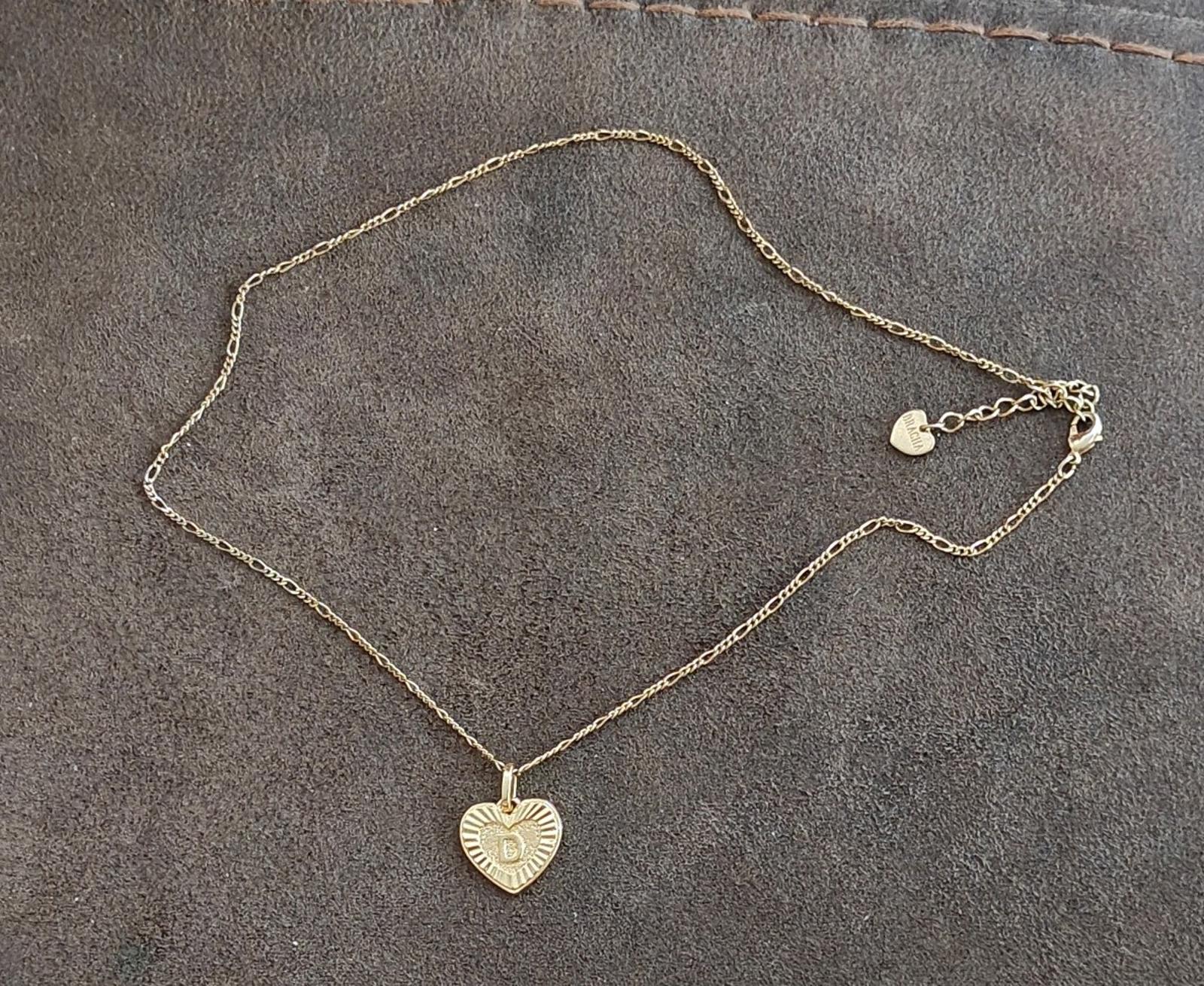 Gold tone heart pendant necklace lying flat on stone background
