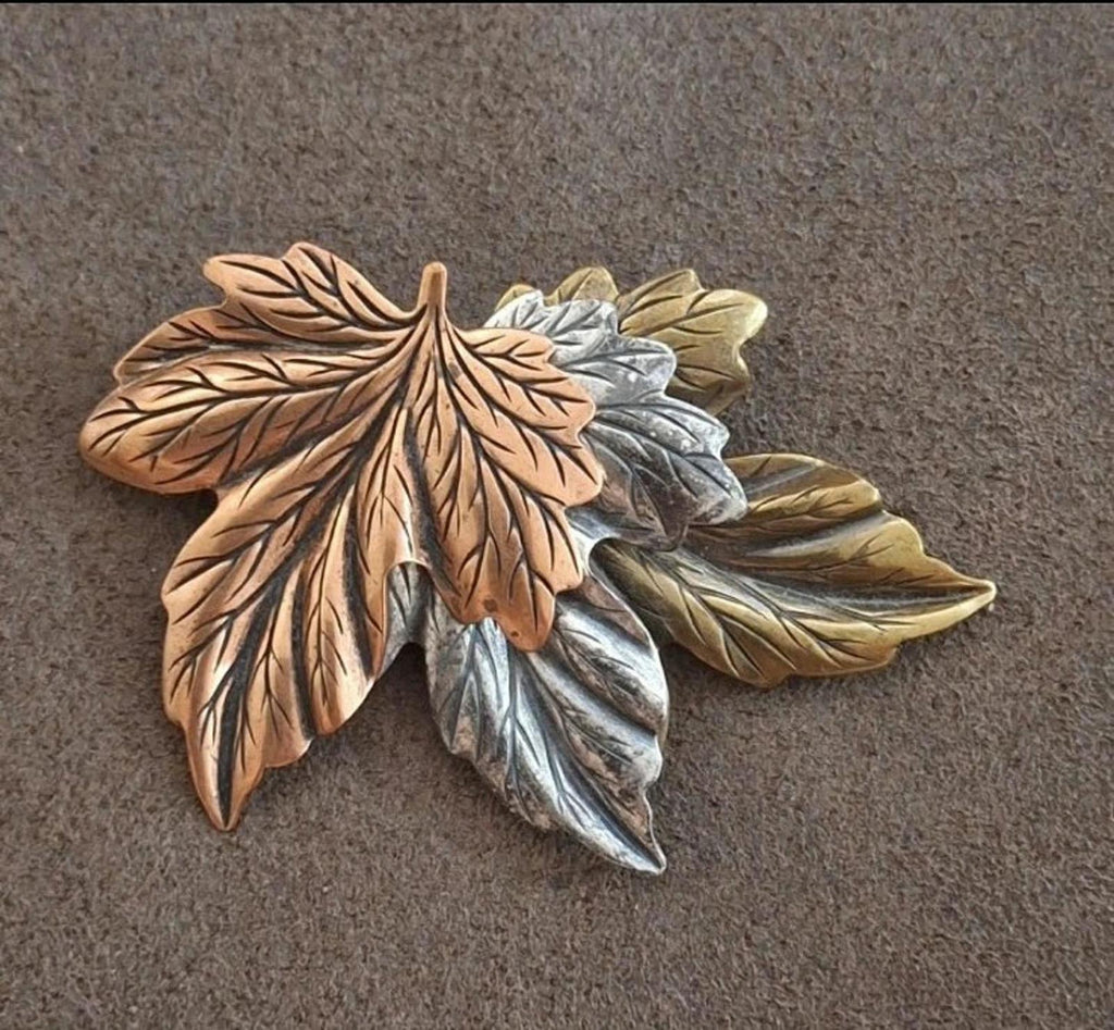 Layered leaf pin brooch with brown, gold, silver, and green-toned leaves on fabric