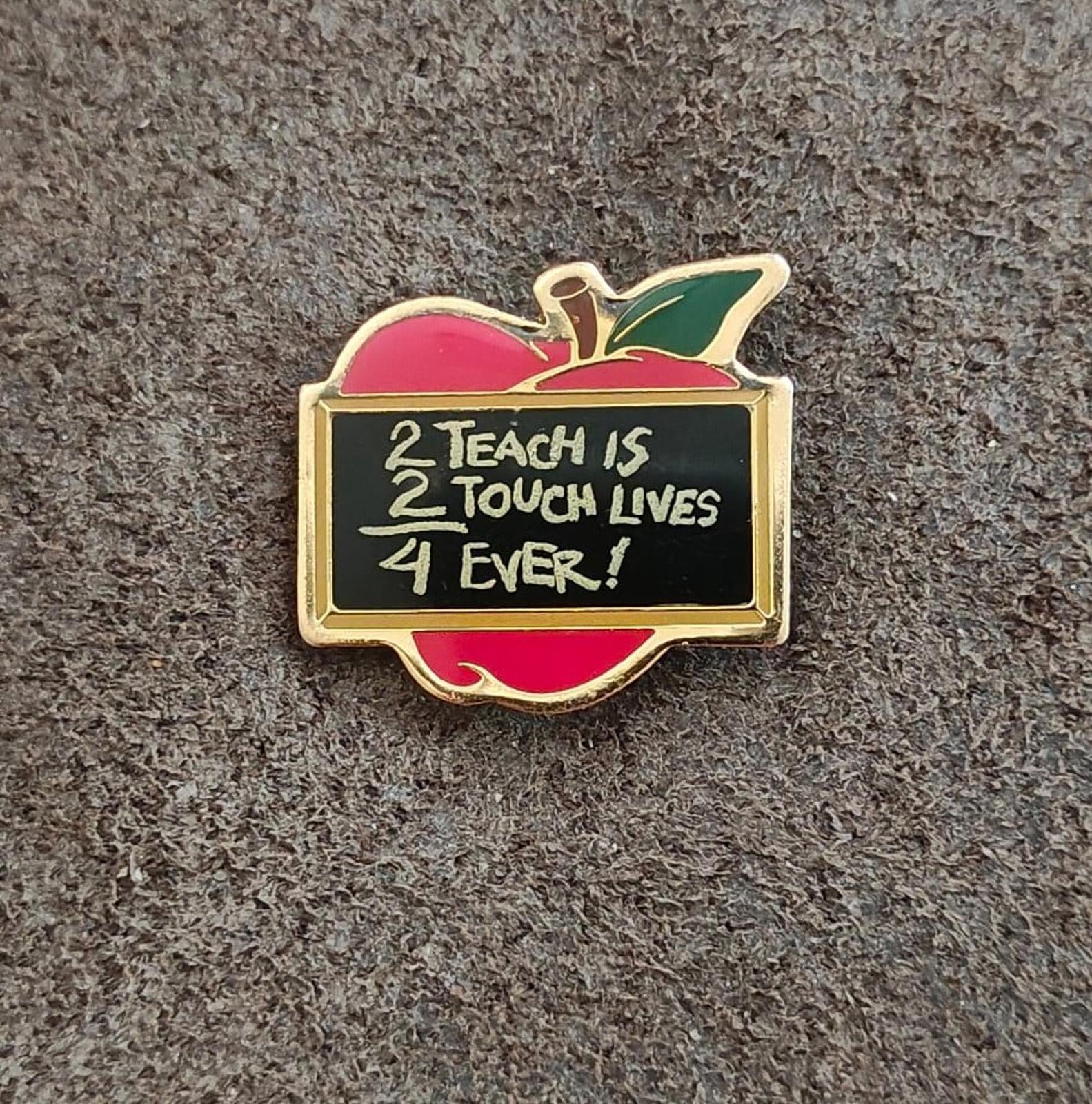 Gold-tone apple-shaped teacher pin with red enamel apple, green leaf, and black message panel