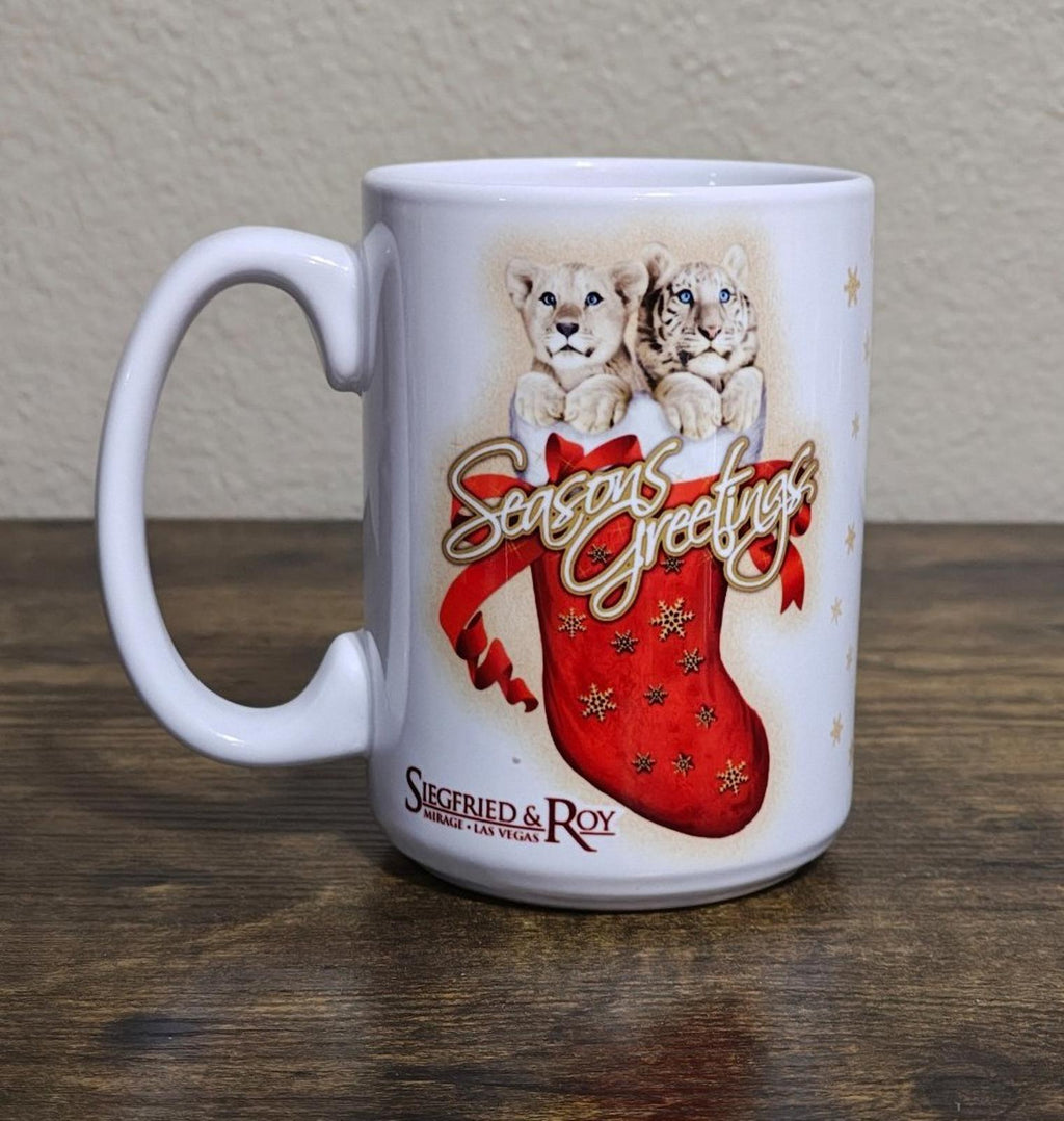 White porcelain mug standing on tabletop with two big cats and red “Seasons Greetings” stocking
