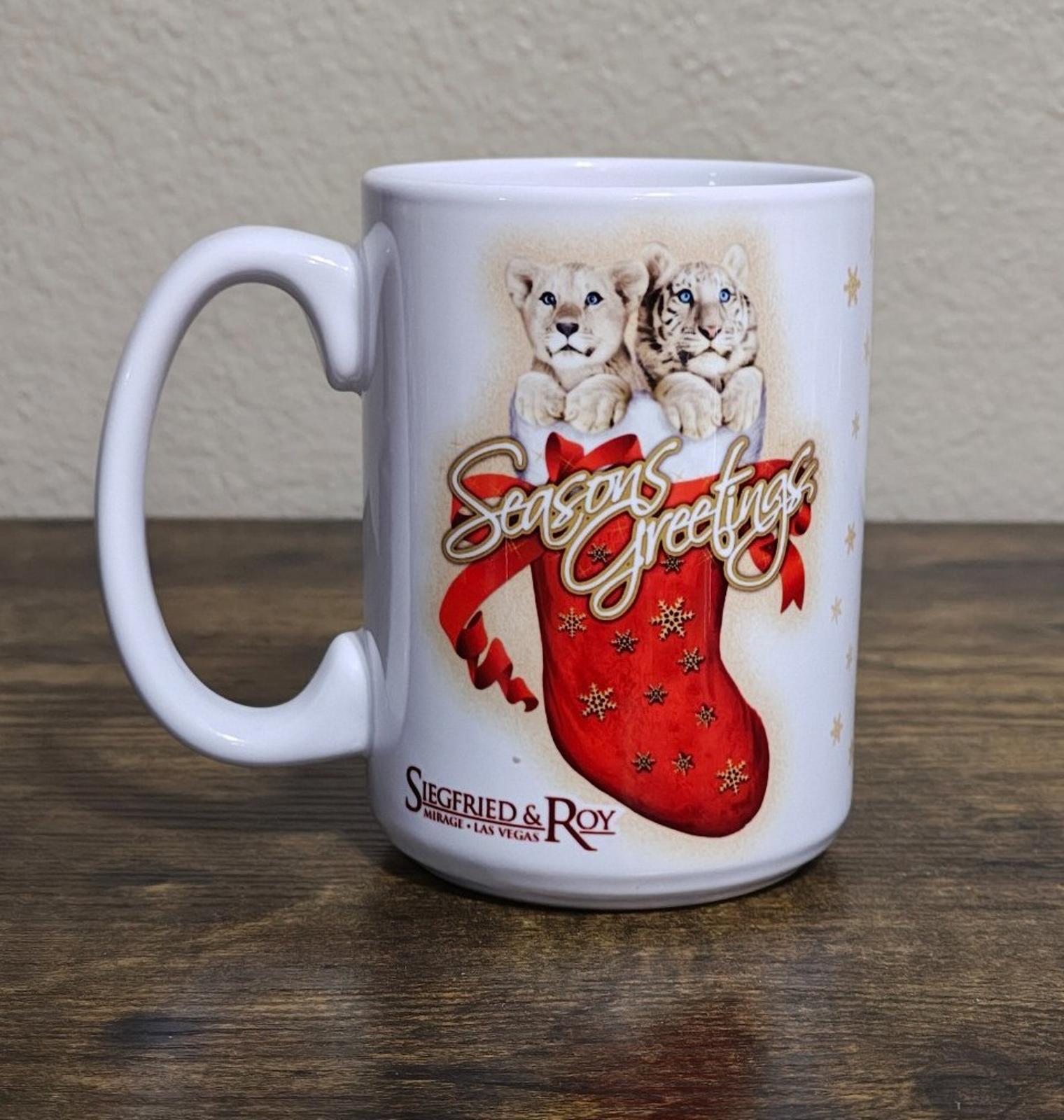 White porcelain mug standing on tabletop with two big cats and red “Seasons Greetings” stocking