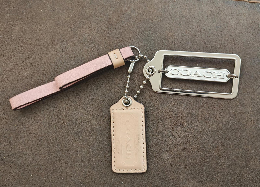 Coach charm keychain with pink strap, metal frame fob, and beige leather hang tag