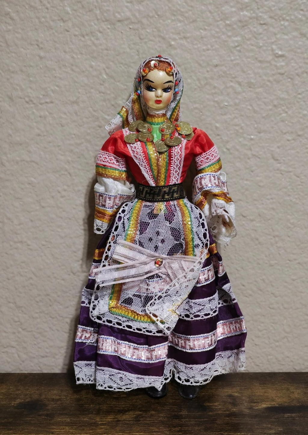Female folk doll full view with red jacket, rainbow trim skirt, and gold coin chest