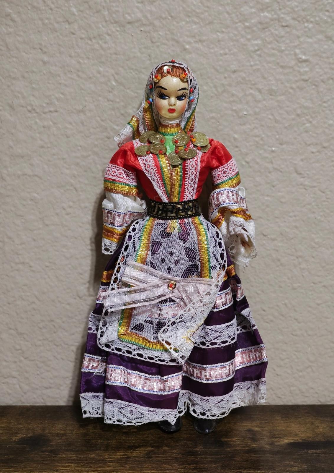 Female folk doll full view with red jacket, rainbow trim skirt, and gold coin chest