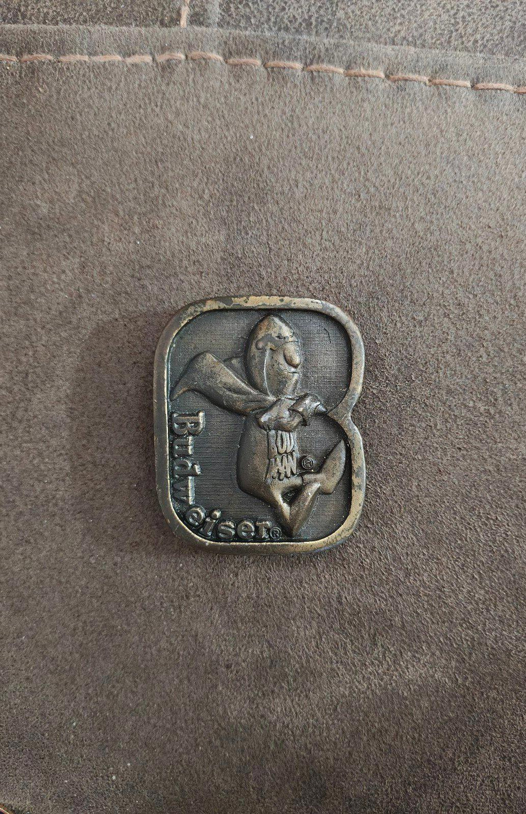 Vintage brass belt buckle front view with character holding a cup; dark antique finish.