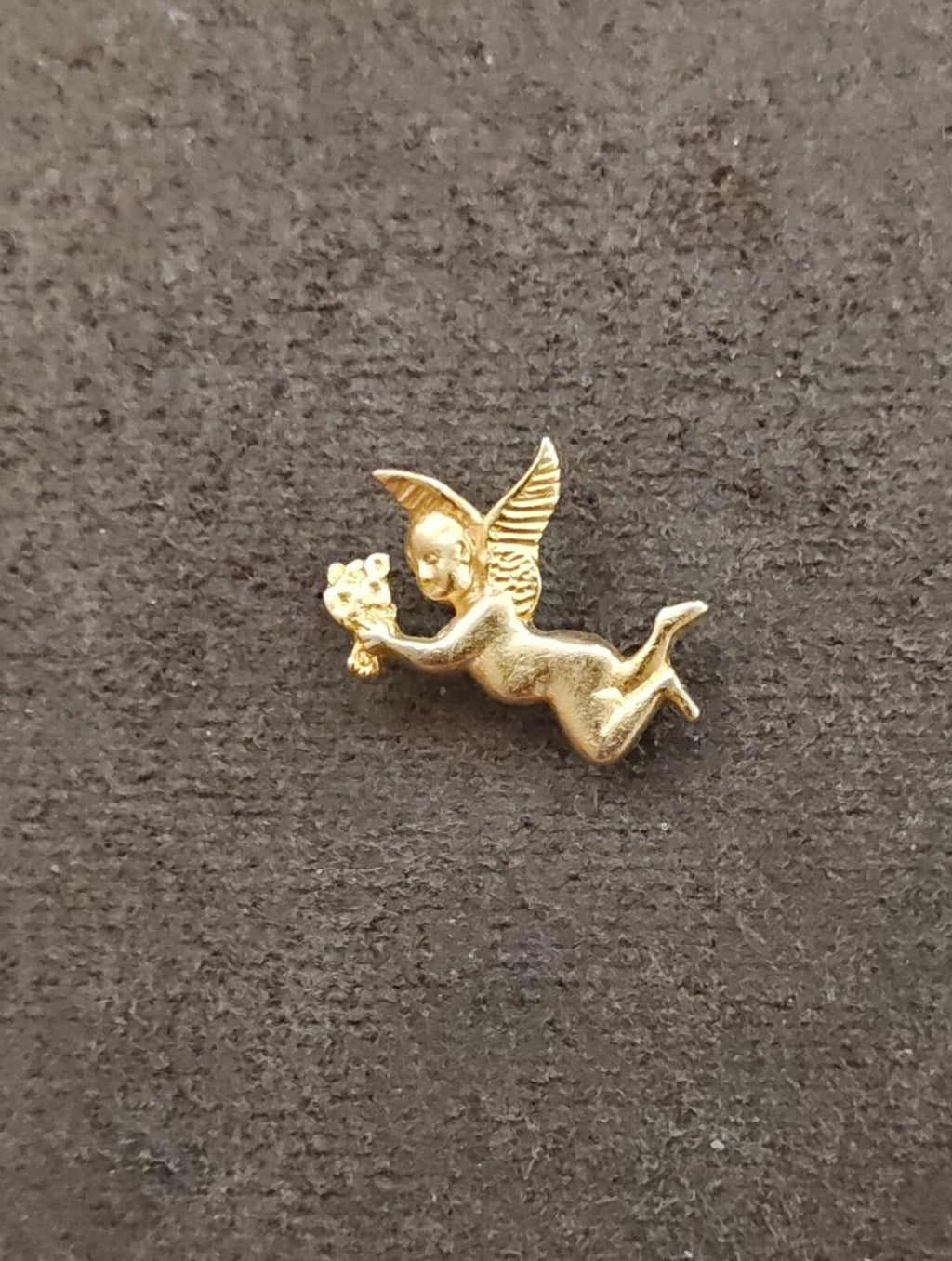 Gold tone flying angel brooch holding flowers, full figure on fabric