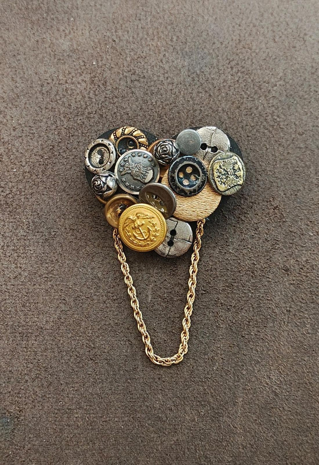 Heart-shaped button collage brooch with gold-tone chain and mixed metal button details