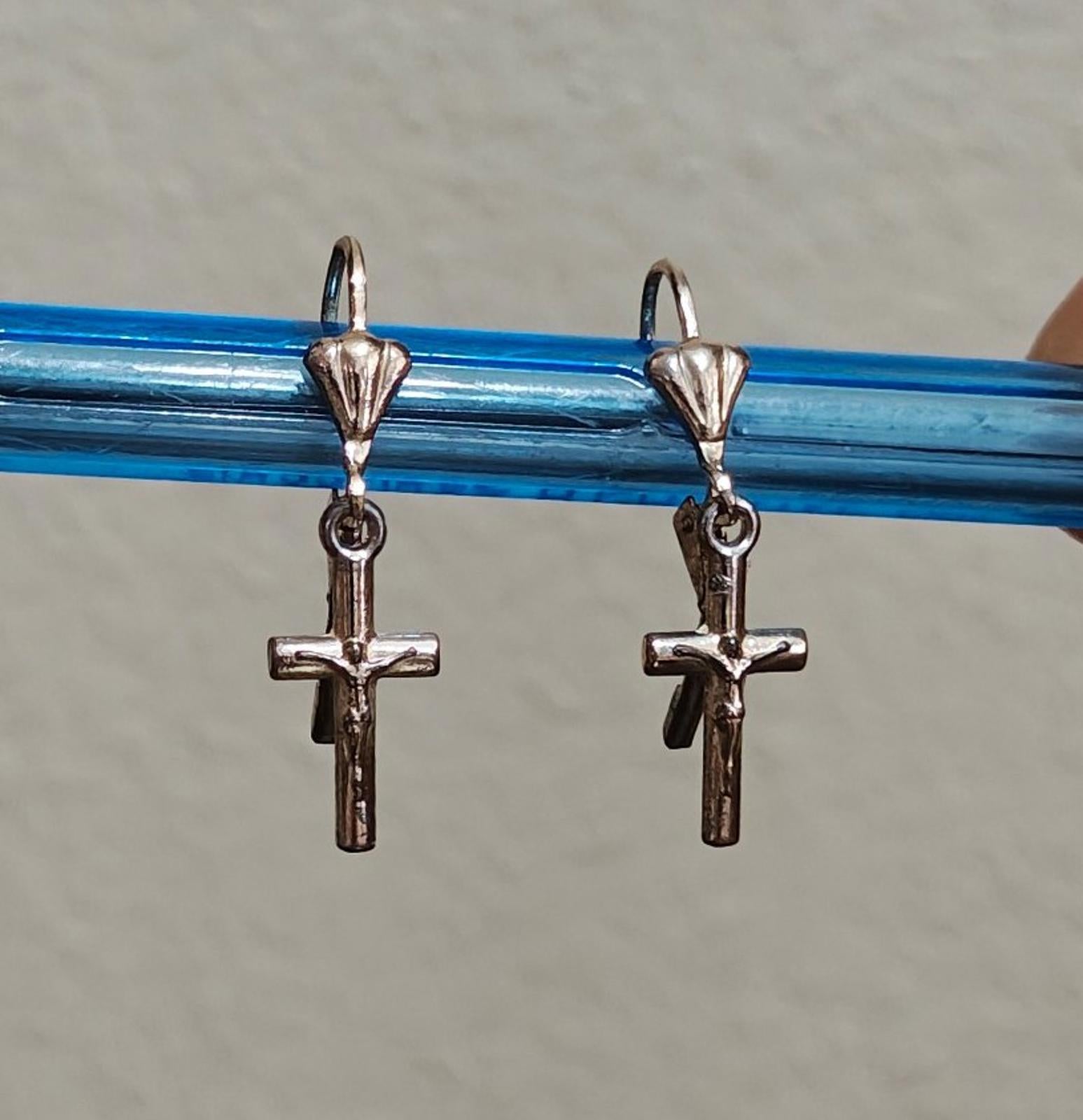 Silver-tone cross dangle earrings with heart tops, shown on a blue bar.