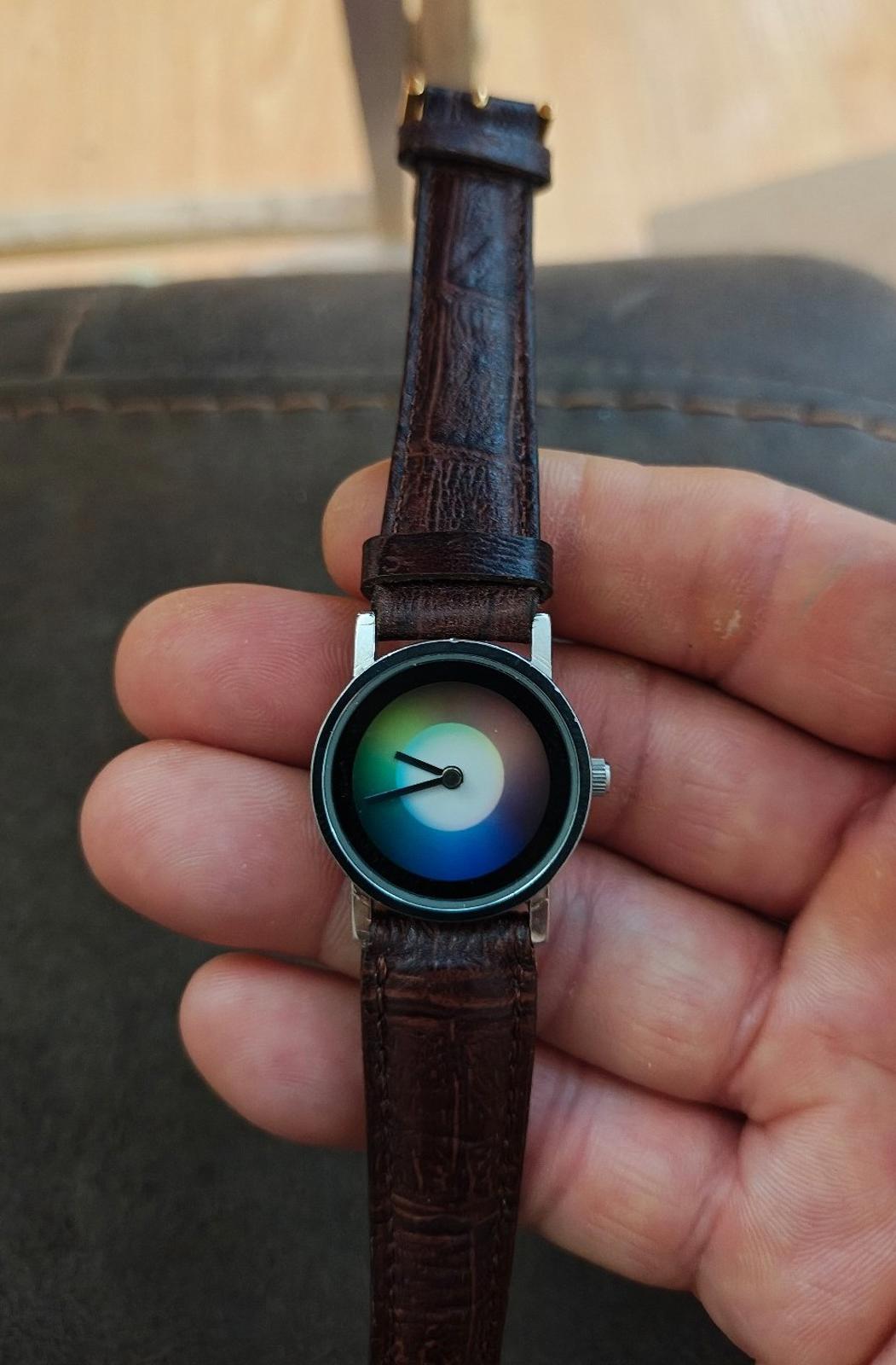 Round dial wristwatch viewed from side, iridescent face, brown leather strap and metal crown