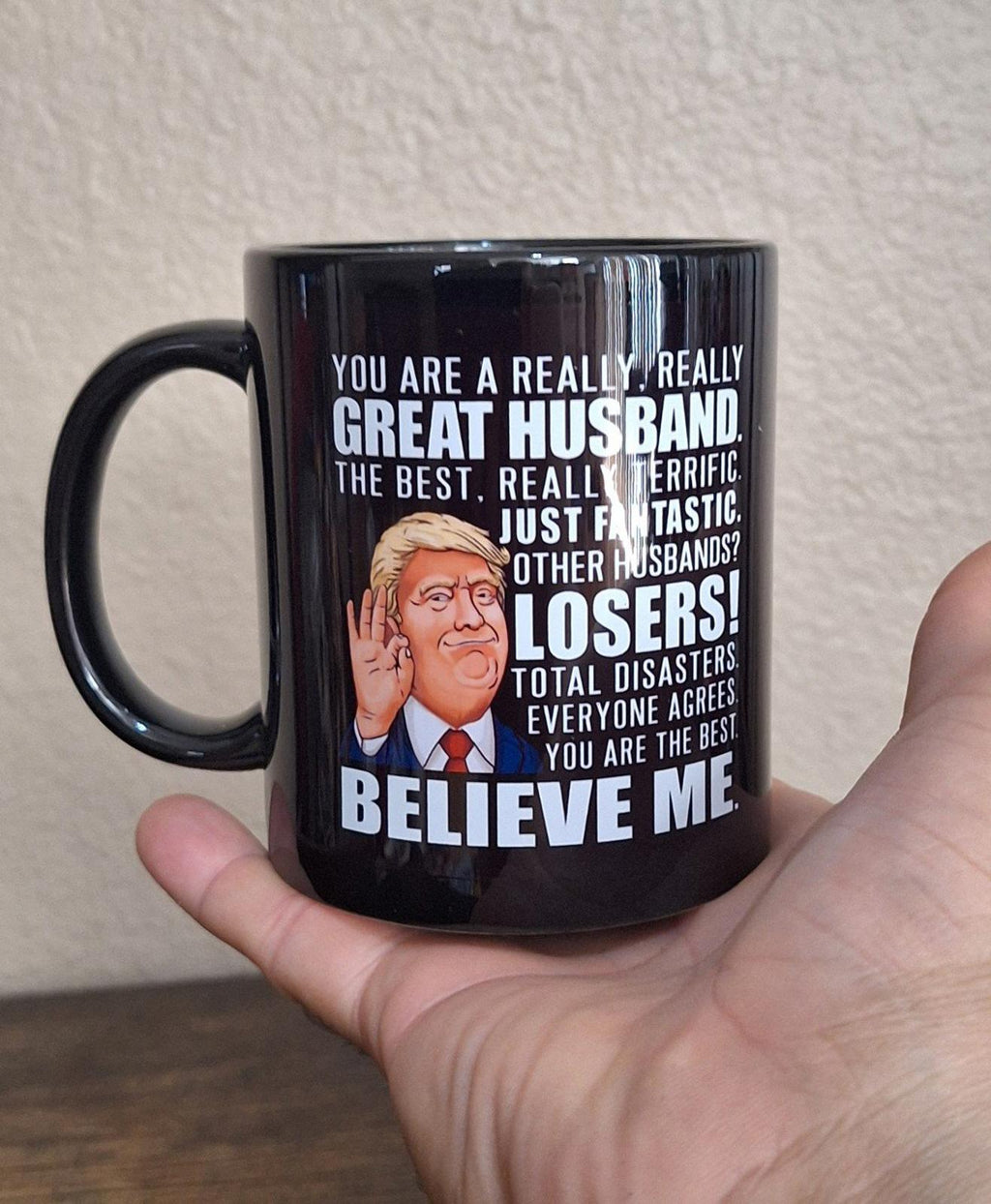 Black ceramic 11 oz mug held in hand, with "Losers" and "Believe Me" graphic