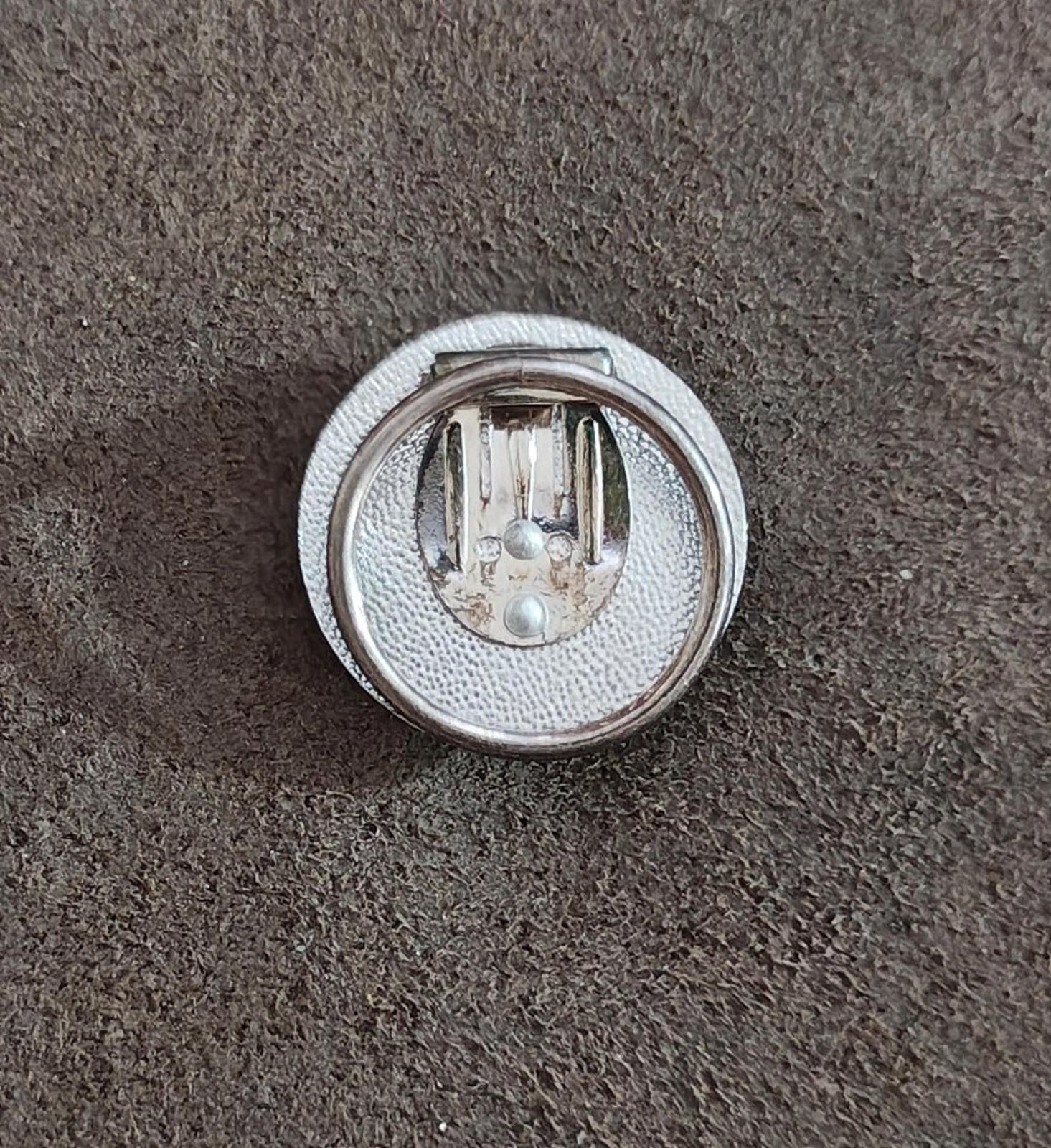 Back view of round silver-tone scarf clip with pin prongs and textured base