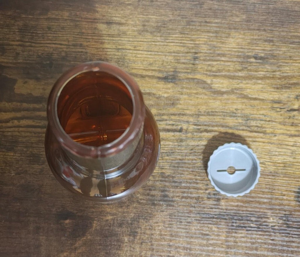 Opened bottle top with white plastic cap and amber liquid inside on wood