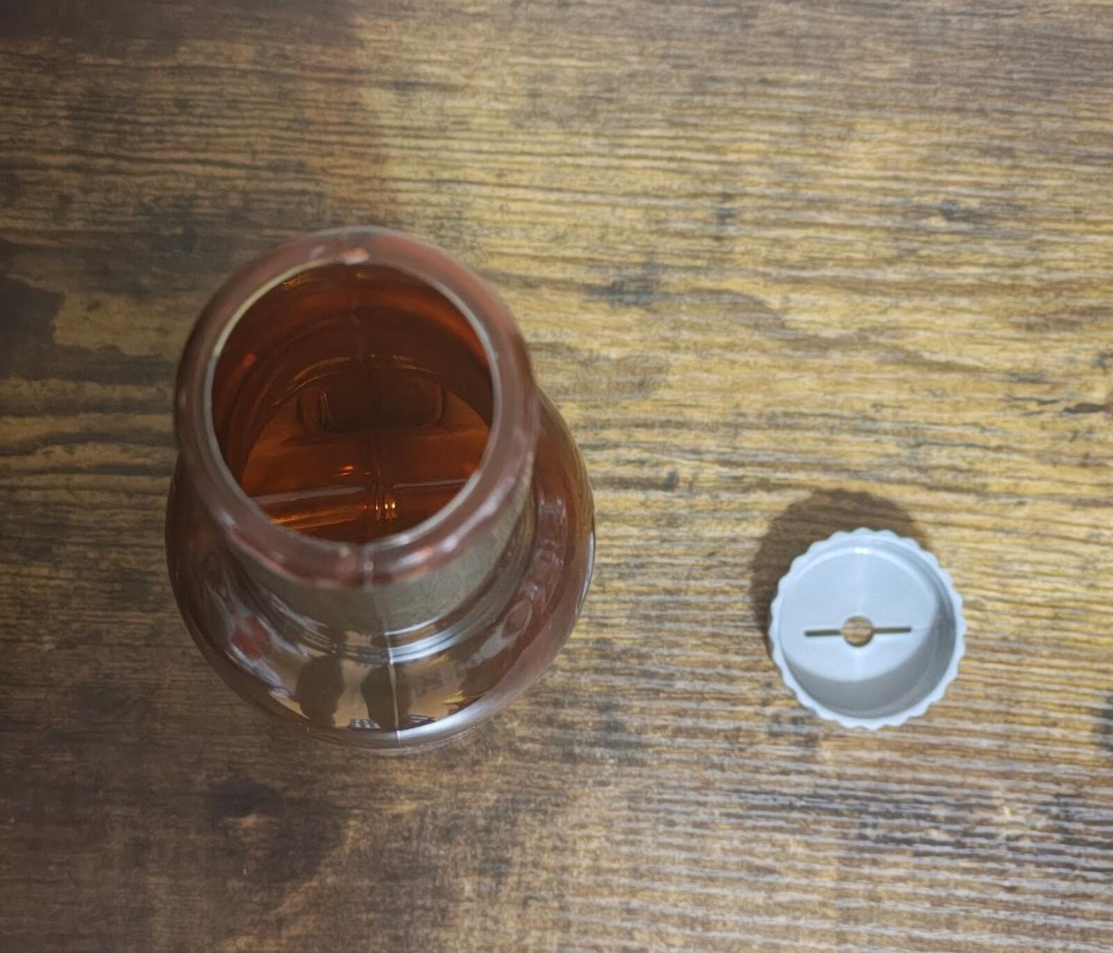 Opened bottle top with white plastic cap and amber liquid inside on wood