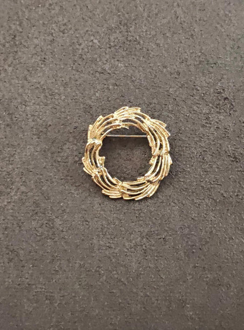 Gold-tone swirling circle brooch with stacked curved ridges, viewed from above