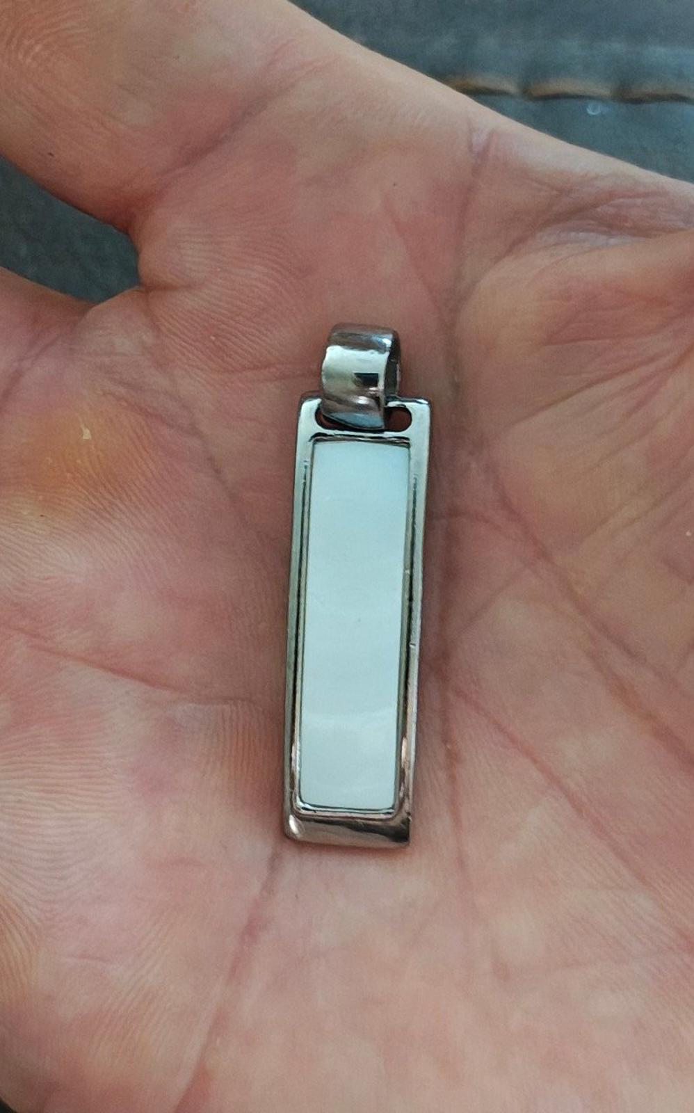 Silver-tone rectangular slide pendant held in hand, light inset window visible.