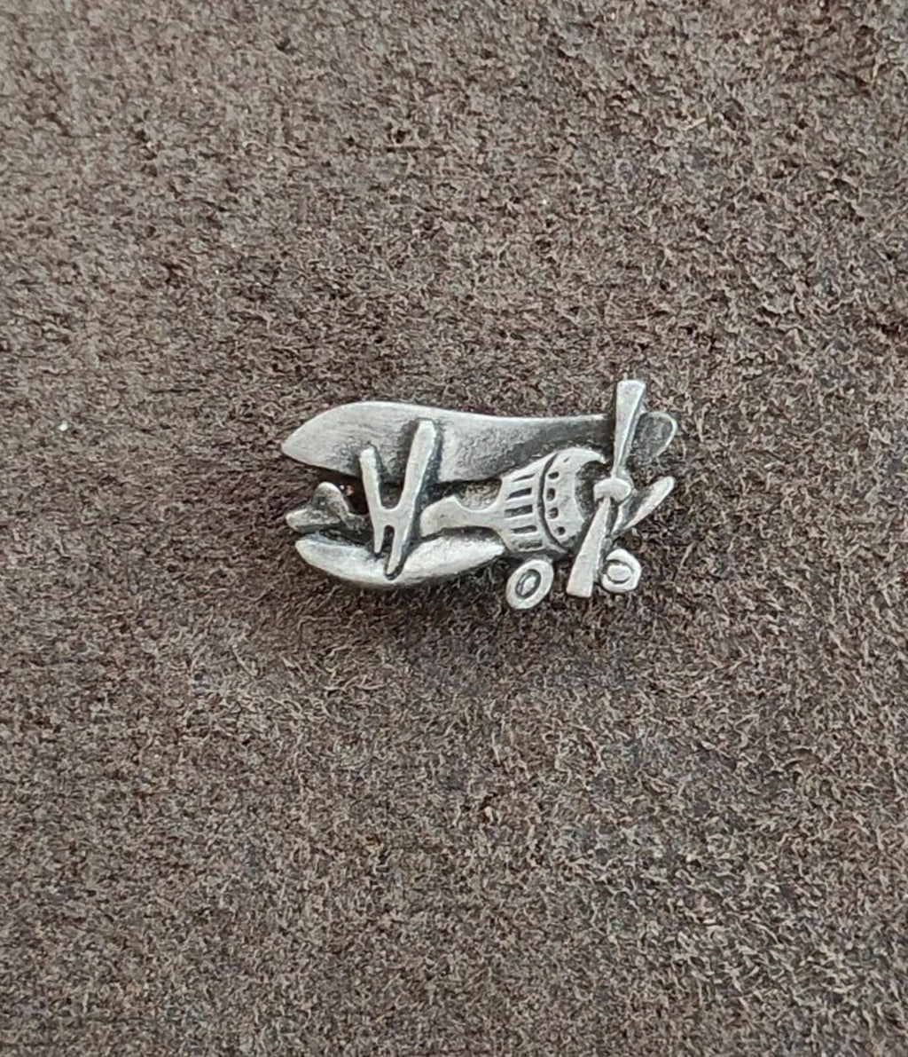 Silver airplane brooch pin on textured surface, side view showing wings and propeller.