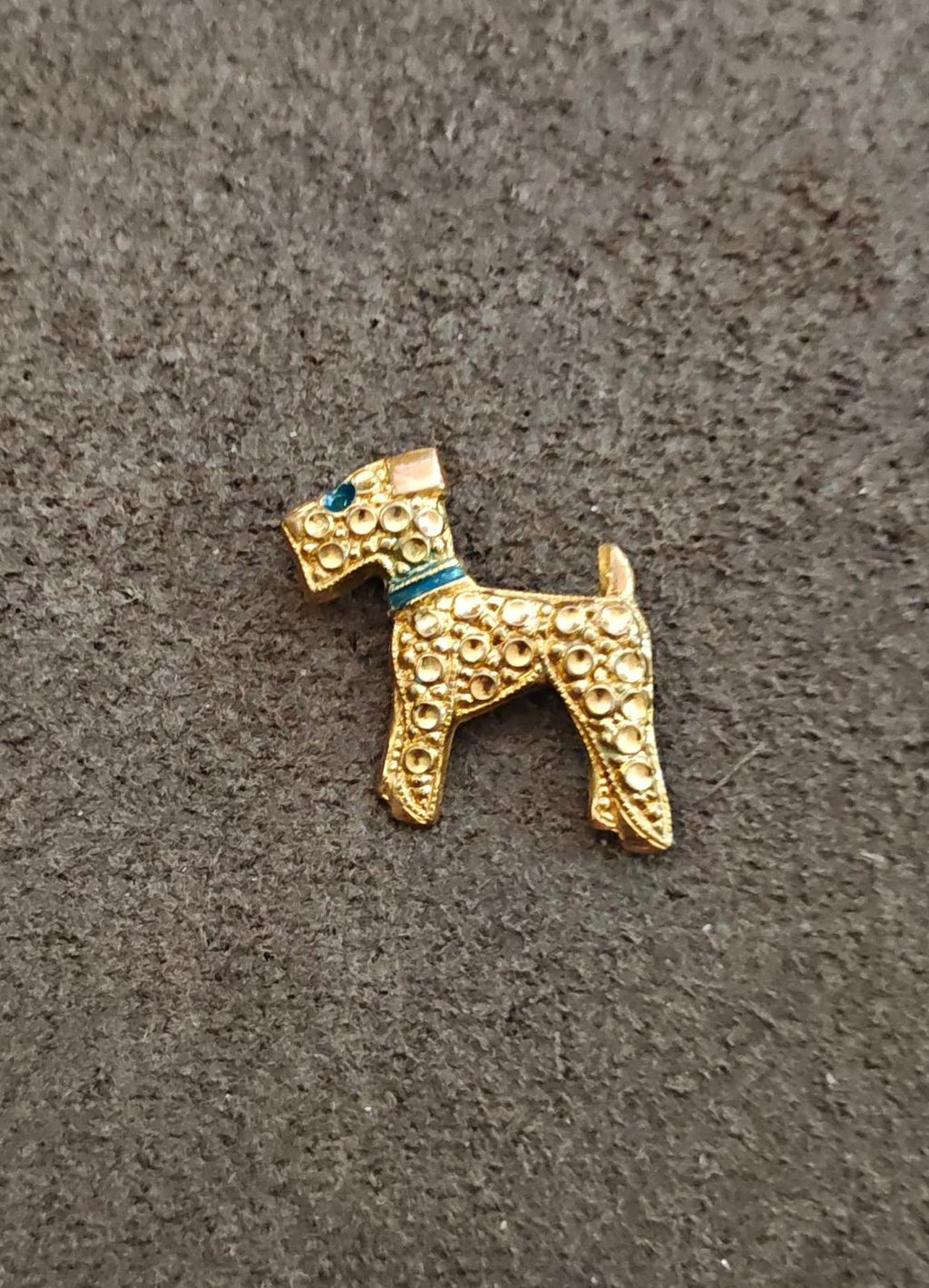 Gold-tone terrier dog brooch with blue enamel eye and collar, ornate circular detailing.